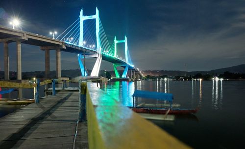 Illuminated suspension bridge over river against sky at night