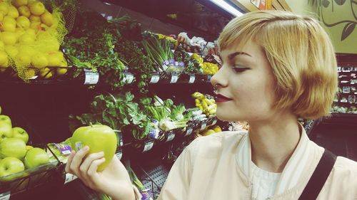 Close-up of blond woman looking at granny smith apple at supermarket