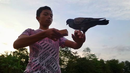 Low angle view of man holding bird on hand against sky