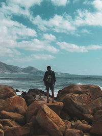 Man standing on rocks at sea shore against sky