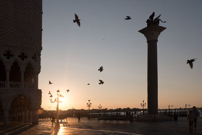 Sunrise in venice with silhouette of the palace of the doges and lantern and flying pigeons