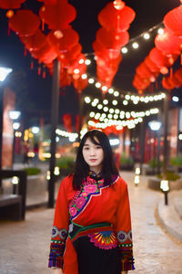 Portrait of woman standing against illuminated lights at night