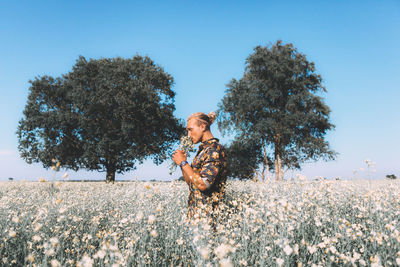 Man smelling flowers while standing against sky