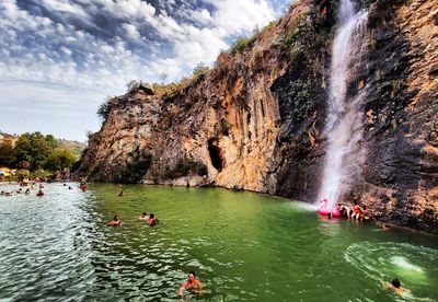 People on rocks in water against sky