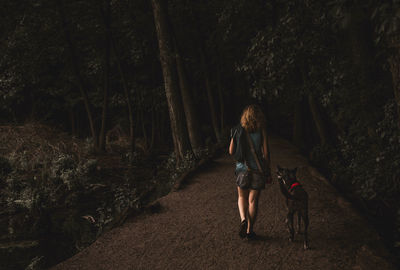 Rear view of woman with dog walking in forest