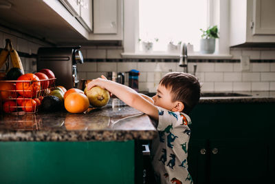Young boy reaching for fruit on kitchen counter