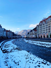 City street by frozen lake against blue sky