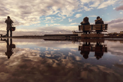 Reflection of people on lake against sky