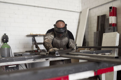 Serious male worker in dirty apron standing at workbench and preparing metal details for welding