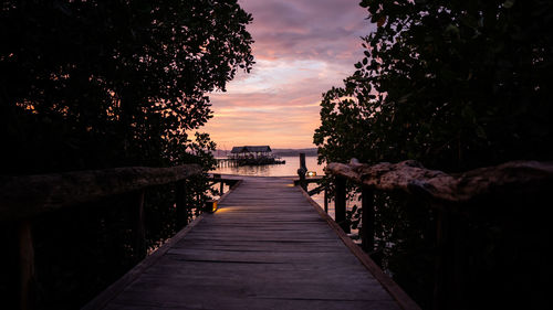 View of pier amidst trees against sky during sunset