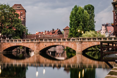 Arch bridge over river amidst buildings in city against sky