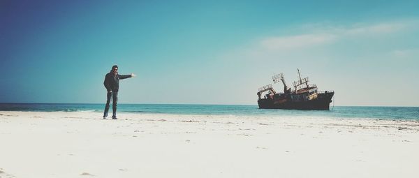 Mid distance view of man pointing towards shipwreck in sea against sky