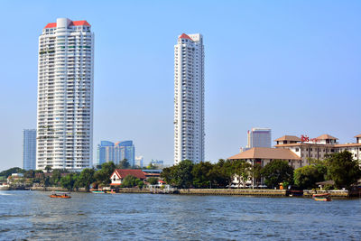 Buildings by river against clear blue sky