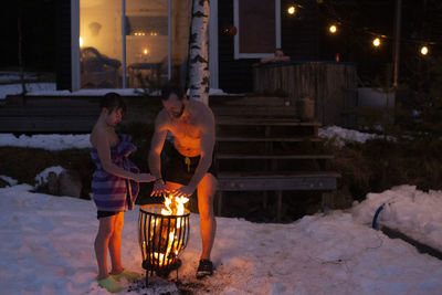 Full length of father and son warming hands at bonfire outside house at night