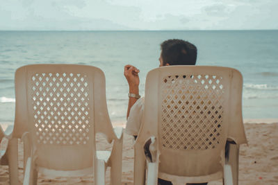 Rear view of people sitting on chair by sea against sky