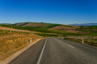 Road amidst agricultural field against clear blue sky