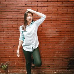 Portrait of young woman standing against brick wall