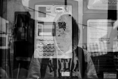 Telephone in booth seen through glass with reflection of person