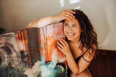 Female painter holding her abstract art on canvas and smiling