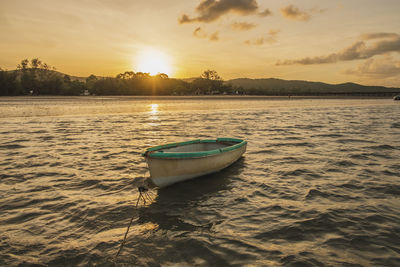 Boat moored on shore against sky during sunset