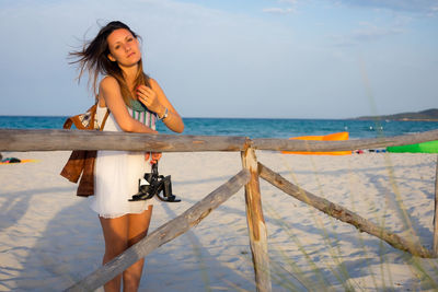 Portrait of young woman standing at beach against sky