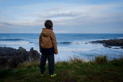 Rear view of boy standing in front of sea against sky