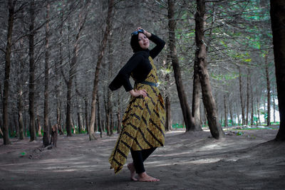 Full length of woman standing amidst trees in forest