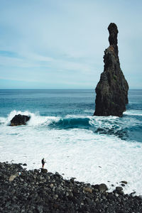 Scenic view of a fisherman on rocks on beach against sky