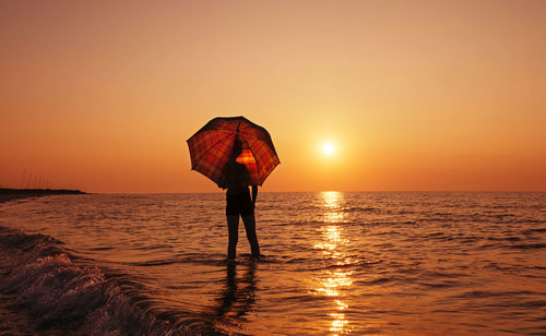 Rear view of woman standing on beach during sunset