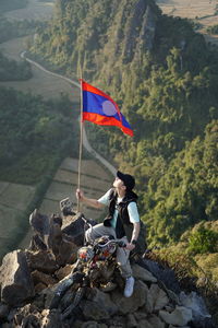 Man holding flag while standing with bicycle on mountain