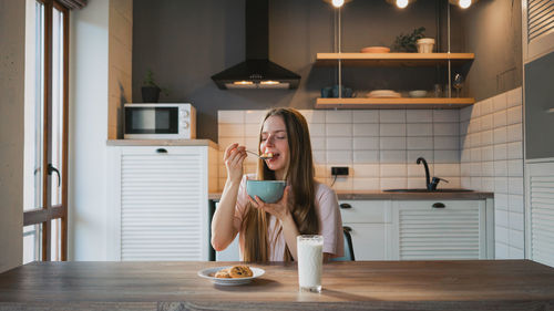 Full length of young woman holding coffee while sitting at table