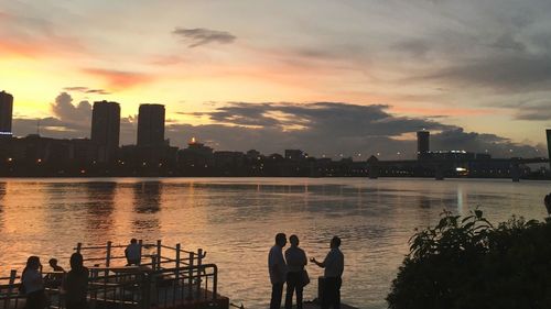 Silhouette people by river against sky during sunset