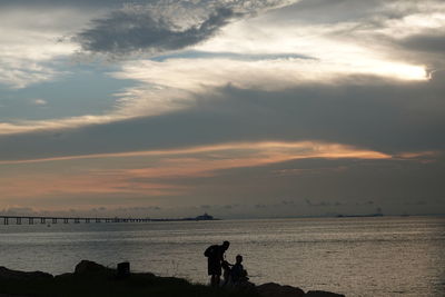 Silhouette people on beach against sky during sunset