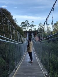 Rear view of man on footbridge against sky