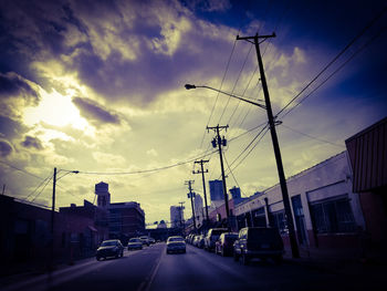 Cars on road by buildings against sky during sunset
