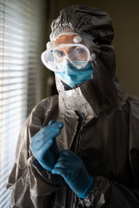 Woman wearing protective suit and mask standing by window