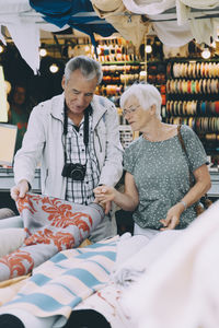 Senior man showing pattern on fabric to woman while shopping at market in city