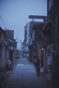 Rear view of girl riding bicycle on street amidst buildings in city