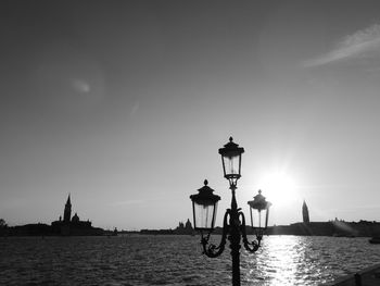 Silhouette street by sea against sky during sunset