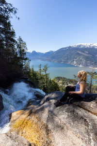 Side view of woman sitting on rock against sky