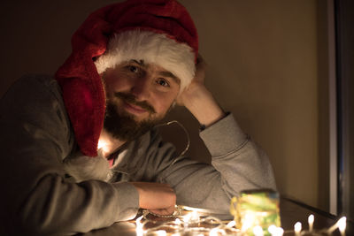 Portrait of man in santa hat with illuminated string light sitting at table