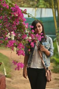 Woman holding pink flower standing against purple flowering plants