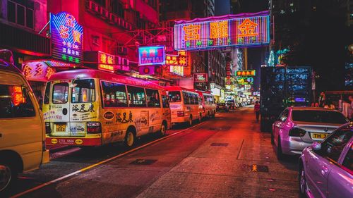 Cars and buses parked on road against illuminated signboard at night