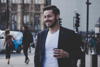 Cheerful businessman holding disposable cup in city