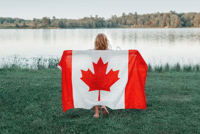 Girl wrapped in large canadian flag by muskoka lake in nature. canada day celebration outdoor. 