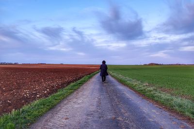 Rear view of woman walking on footpath against cloudy sky