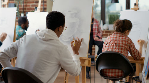 Rear view of man sitting on chair against canvas