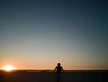 Silhouette man standing on street against sky during sunset