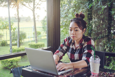 Young woman using mobile phone while sitting on table