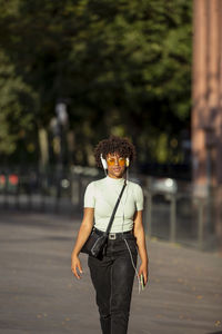 Stylish dark-skinned curly young brunette in yellow sunglasses enjoys music in headphones while